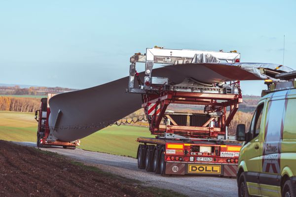 Transport lourd d'une pale d'éolienne sur un camion-remorque spécialisé de DOLL sur une route de campagne.