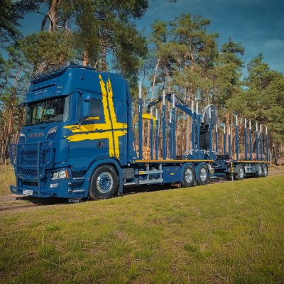 Camion bleu avec remorque à plate-forme DOLL sur une route de campagne ensoleillée lors du chargement.
